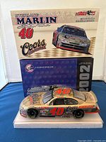 Front angled view of the diecast model car with box and advertising backdrop showing the Sterling Marlin 40 Coors Original model and branding