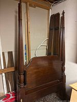 Four poster wooden bed frame shown from front angle, showing tall posts, headboard with curved top, and dark brown finish.