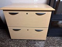Front view of a light wood finish two drawer lateral file cabinet with black handles and key lock in center of each drawer.