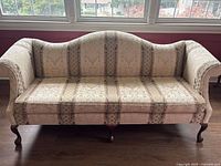 Front view of vintage beige patterned fabric sofa showing scalloped backrest and cabriole legs