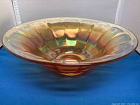 Side view of iridescent marigold vintage Fenton carnival glass bowl with scalloped edge on blue background.
