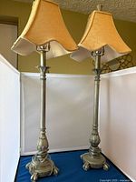 Pair of vintage metal table lamps with silver bases and beige bell-shaped shades shown side by side against a white backdrop.