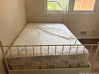 Full view of the white metal full-size bed frame with mattress covered by a fitted white sheet.