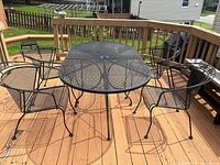 Five-piece wrought iron mesh patio set on wooden deck showing table and four stackable chairs with cushions