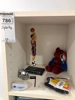 Front view of the shelf showing the Andrea Bargnani figurine, plush bear, Raiders helmet, and other memorabilia items.