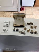 Six pairs of men's cufflinks laid out including one pair in a box labeled sterling silver.