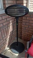 Full view of the freestanding black outdoor electric heater with circular base, adjustable pole, and protective grille.