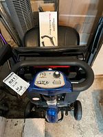 Top view of Drive mobility scooter handlebar and control panel with battery indicator and speed dial, key ignition present. Includes boxed Challenger Deluxe rear view mirror on scooter seat.