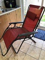 Red fabric patio lounger unfolded showing reclining position and headrest cushion attached.