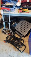 Three folding hand trucks/utility carts: Magna Cart hand truck with red handle extended; smaller black utility cart; folding cart with slotted plastic platform folded