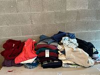 Overview of assorted men's clothing items folded and stacked, containing shirts, sweaters, and jeans in varied colors such as red, beige, blue, and green.