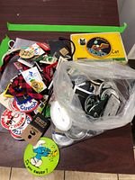 Top overview showing the yellow Apollo 11 Centennial cigarette tin, numerous collectible pins, buttons, and lanyards grouped on a table.