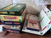 Stack of six Monopoly themed board games boxed: The Legend of Zelda, Monopoly Canada, Monopoly Looney Tunes, Monopoly Nintendo, and Monopoly Star Wars visible.