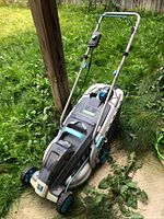 Full view of the Redback battery operated lawn mower on grass near a wooden post showing its overall design and condition.