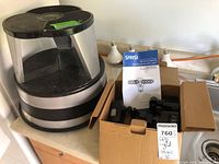 Photo of the lot showing a black round gray step stool and an open box containing the SANSI LED security light with user manual.