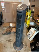 Seville Classics tall dark gray tower fan with vertical vents and cord visible on the concrete floor in a garage setting.
