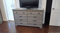 Front view of gray dresser with television on top, showing six drawers and handles.