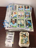 Photo showing several baseball cards of Toronto Blue Jays players stored in plastic sheet pages in binders, and loose cards stacked with rubber bands on a wooden surface.