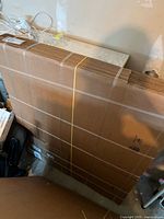Stack of flat packed corrugated cardboard boxes bundled with tape and yellow straps, shown standing upright in a garage space.