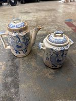 Photo showing front and side view of the ceramic teapot and sugar pot with lids, displaying blue and white pastoral scene transferware decoration on ivory base.
