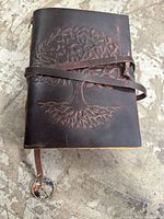 Front cover of brown leather journal with embossed tree and strap closure visible