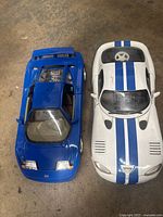 Top view of two diecast model cars, featuring a blue Bugatti 110 EB model on the left and a white model next to it, showing overall size and condition.