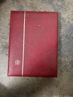 Red textured cover of the stamp album with gold stripe and emblem.