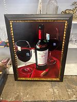 Framed giclee print artwork featuring wine bottle and glasses on red background in wood frame with gold inner border.