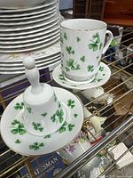 Photo of porcelain shamrock bell, cup, and saucer on a shelf showing pattern and form.