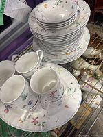 Photo showing stacked plates, bowls, and mugs with floral and butterfly design and blue border on white ceramic.