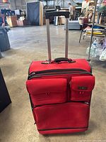 Front and top view of large red suitcase with extended telescoping handle, showing three front pockets and two carry handles.