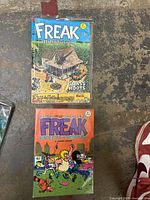Photo of two Fabulous Furry Freak Brothers comic books, Issue No. 5 titled 'Grass Roots' on top and another issue below with an orange cover showing characters running.