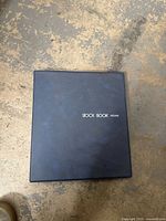 Closed black Stock Book Deluxe showing the front cover on the floor.