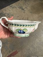 Side view of ceramic gravy boat showing white base with green trim and fruit illustrations.