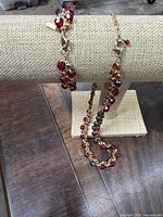 Bracelet and necklace displayed on beige fabric stand showing the colorful faceted glass beads in red, gold, and blue with gold-tone chain links and clasps.
