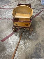 Front view of vintage toy wagon showing wooden bench seat, handle, and front wheels.