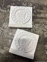 Two white plaster Mayan Aztec zodiac plaques shown from the front with detailed raised circular zodiac motifs and patterned borders.