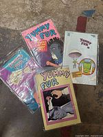 Four Yummy Fur comic book issues with varying vibrant cover illustrations, placed on a concrete floor.