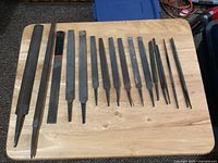 Photo of 17 assorted hand files laid out on a wooden surface, showing different shapes and sizes.