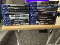 Stacked PS4 game cases showing spines and titles in two piles on a wooden table.