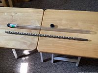 Single long carbide tip drill bit laid out on two wooden tables next to a clear plastic storage tube with a black cap.