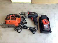 Photo shows three tools: Black & Decker corded jigsaw, Craftsman corded drill, and Black & Decker Crosshair laser level in soft case.