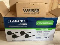Box containing four-pack Weiser Elements passage door handles with branding and features displayed