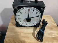 Front view of Gra Lab darkroom timer showing large numbered dial, pointer hands, and attached power cord.