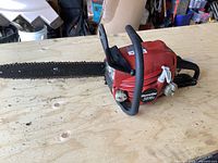 Full view of the Homelite 3816c chainsaw showing red body, black handle, and 16-inch blade with chain attached. The saw is placed on a wooden surface.