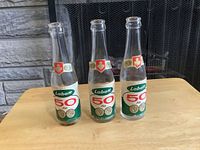 Three vintage Labatt 50 Ale mini bottles standing upright on a wooden surface in front of a fireplace. Labels show Labatt logo, 50 Ale text, and Canadian maple leaf emblem. Bottles are clear glass, about 8 inches tall.