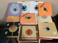 Top view of 45 rpm vinyl records in various paper sleeves, showing labels including CBS, Columbia, A&M, and others.