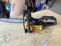 Full side view of a yellow and black McCulloch chainsaw placed on a wooden surface showing the metal cutting bar with chain, front handle, and engine housing.