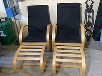 Pair of bentwood armchairs with curved natural wood arms and black fabric upholstery with two bentwood ottomans placed in front of them.