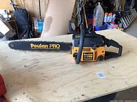 Side view of orange and black Poulan Pro chainsaw on wooden surface, showing overall form and bar length